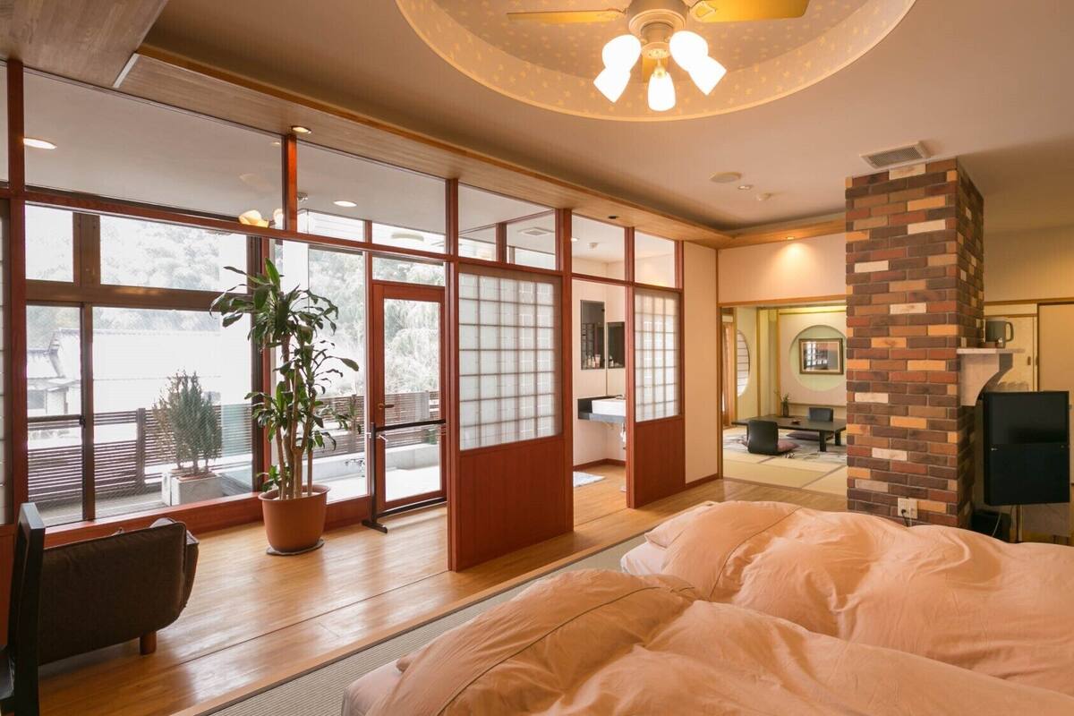 A bedroom with a large bed, sliding glass doors, a potted plant, and a brick fireplace.