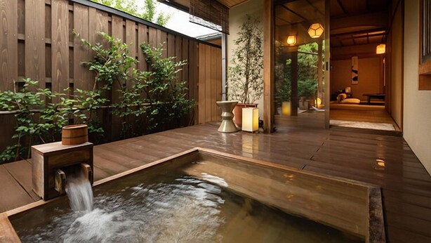 Eine Holzterrasse mit einem kleinen Wasserspiel und Topfpflanzen.