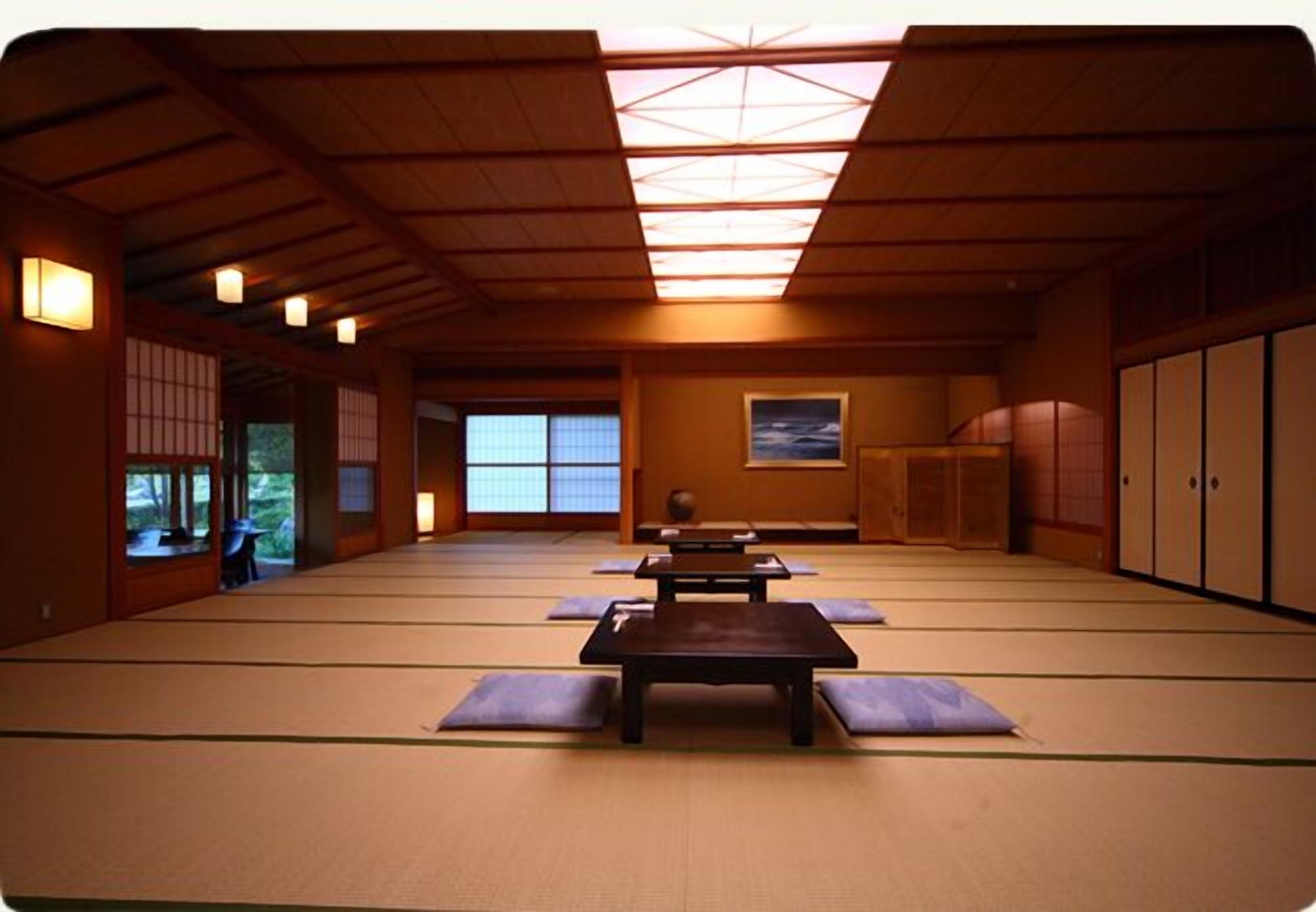 Una habitación con esteras de tatami, vigas de madera y una baja mesa con cojines.