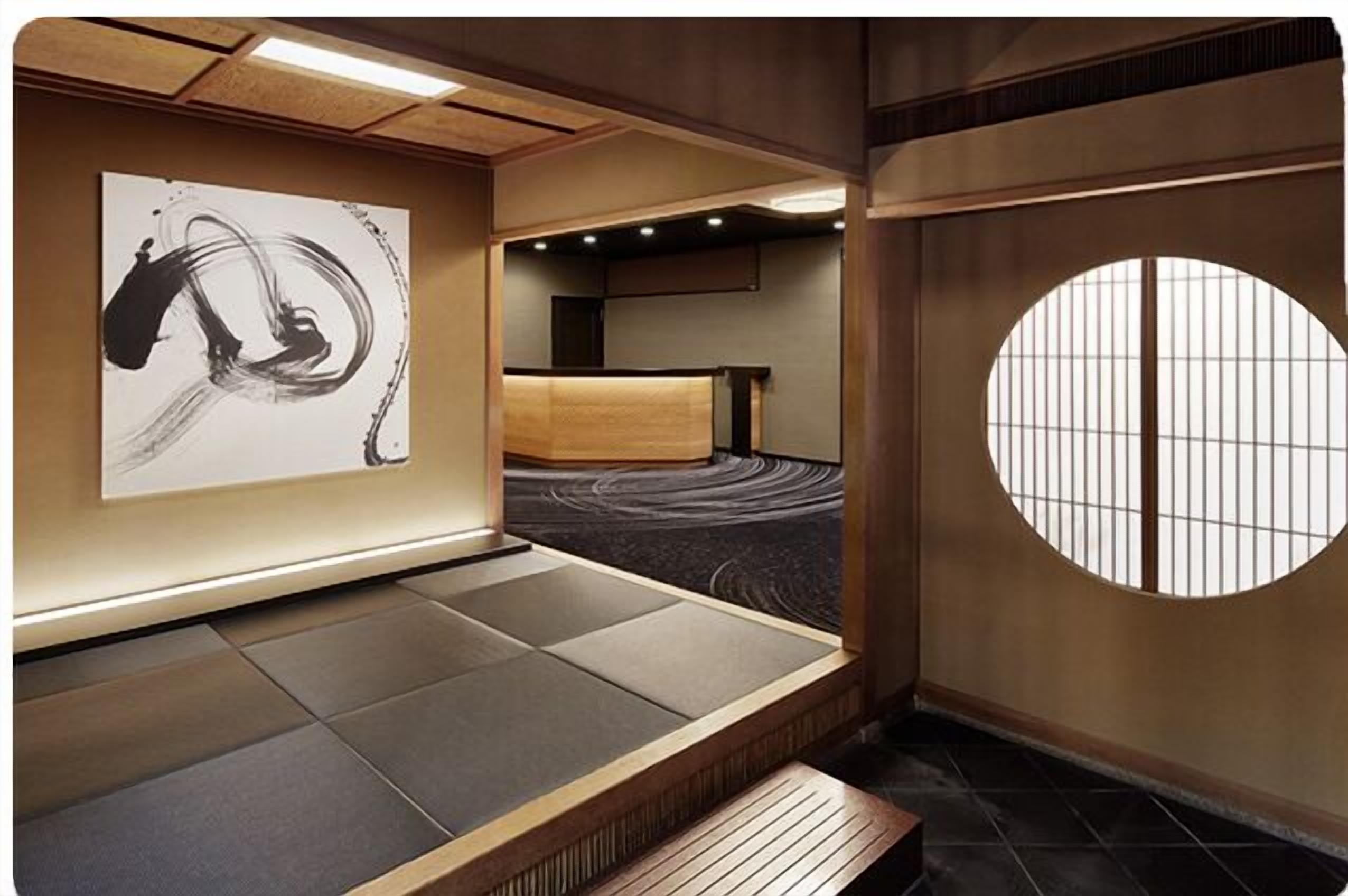 Una habitación tradicional japonesa con suelo de tatami, un banco de madera bajo, un futón de tatami, un biombio shoji y un cuadro abstracto blanco y negro en la pared.