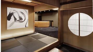 Una habitación tradicional japonesa con suelo de tatami, un banco de madera bajo, un futón de tatami, un biombio shoji y un cuadro abstracto blanco y negro en la pared.