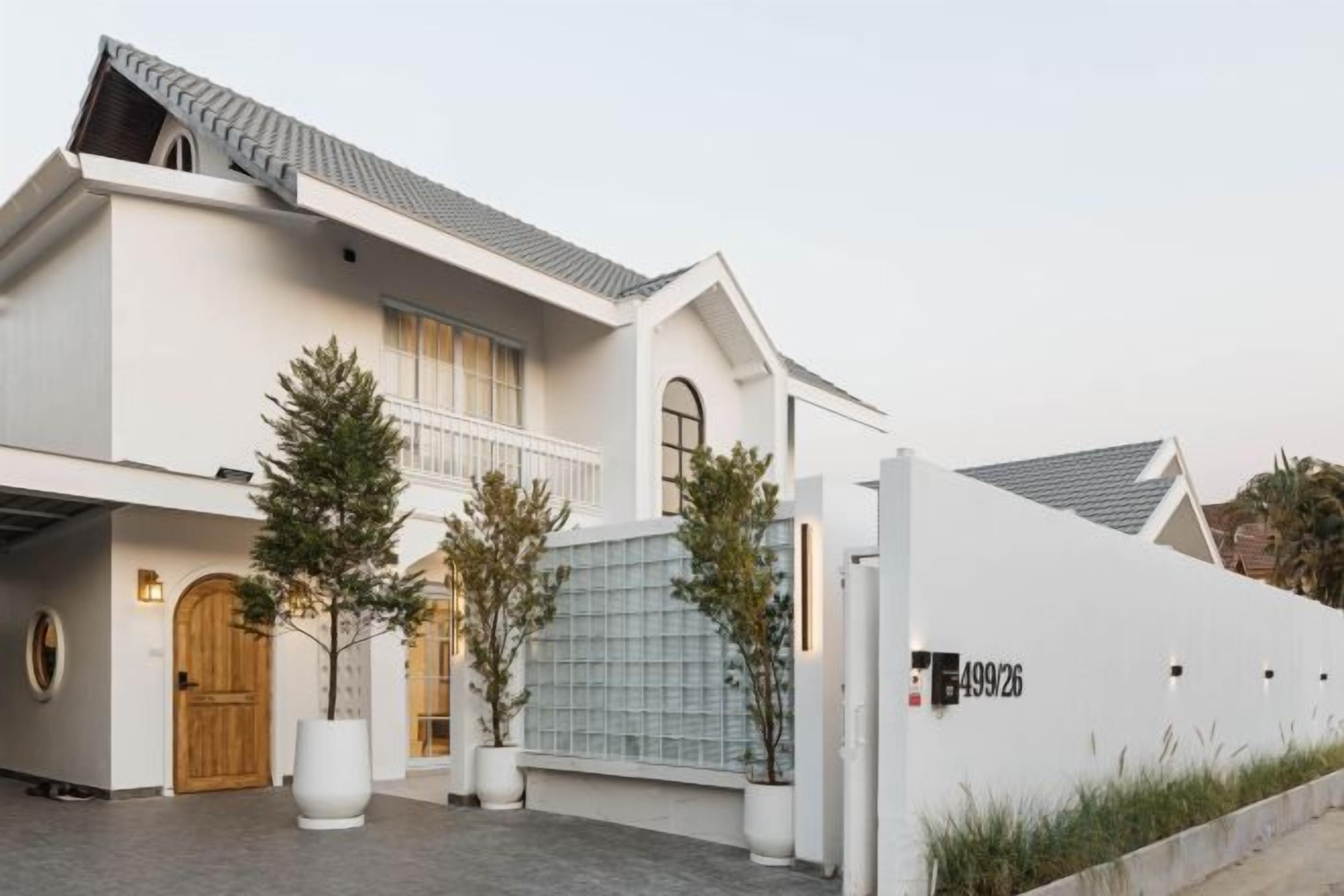Un edificio de dos pisos con fachada blanca, una puerta de madera y un acceso con reja.