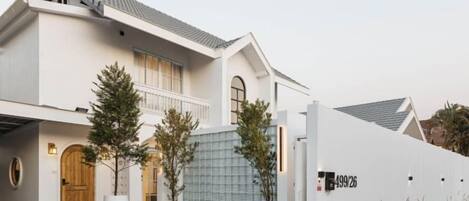 Un edificio de dos pisos con fachada blanca, una puerta de madera y un acceso con reja.