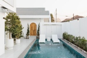A swimming pool with lounge chairs, a wooden door, and potted plants. - Zenzen Pool Villa (San Sai)