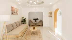 A modern living room with a sofa, a small round table, and a ceiling light fixture. - Zenzen Pool Villa (San Sai)
