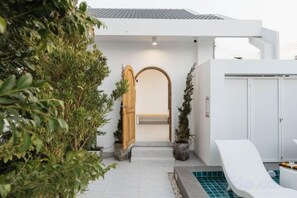 Un edificio moderno con fachada blanca, puerta de madera y zona de piscina con tobogán.