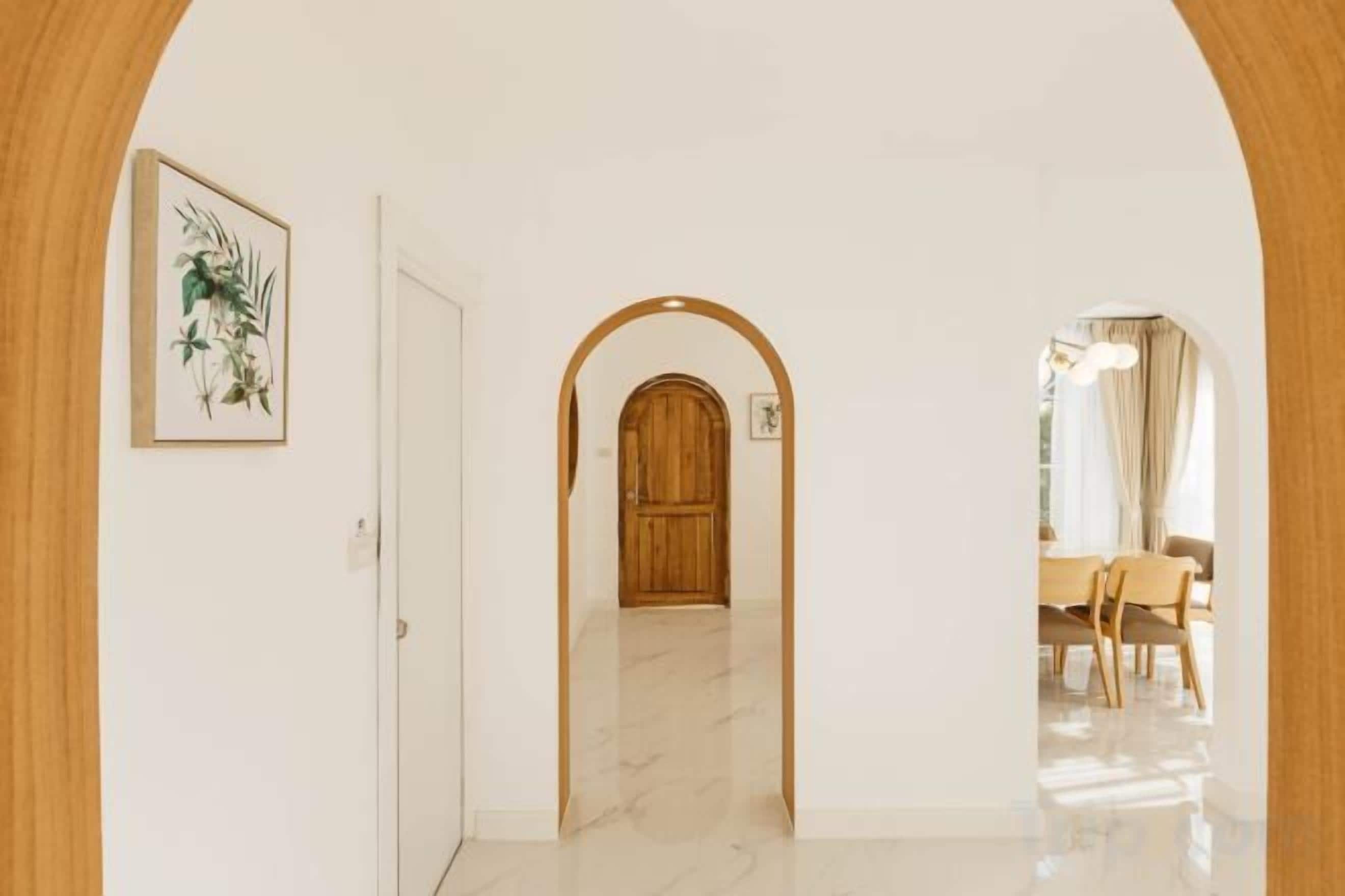 A hallway with a wooden door, a framed picture, and an arched doorway leading to a dining area.