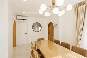 A dining area with a wooden table and chairs, a round mirror on the wall, and a ceiling light fixture.