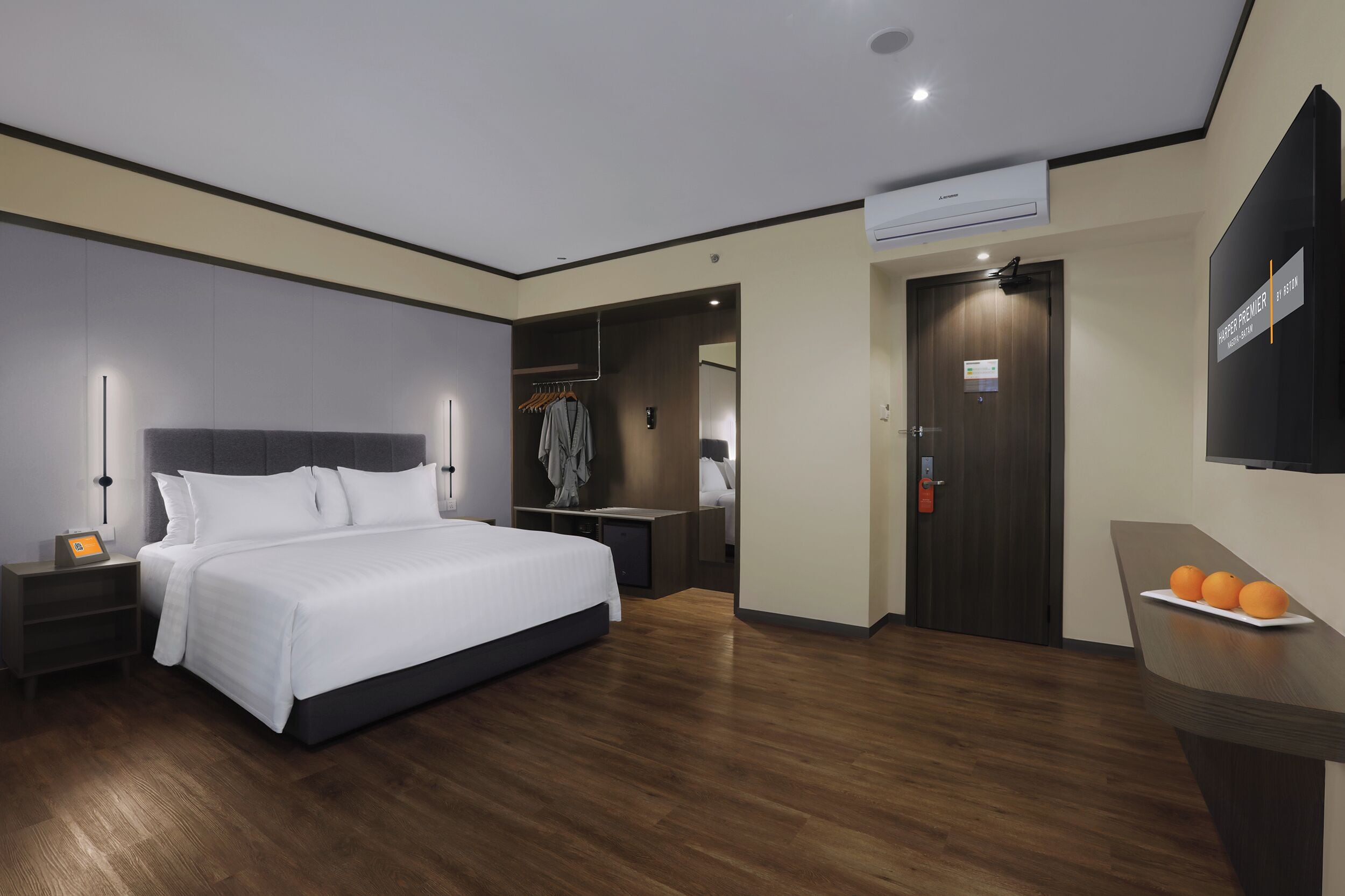 Una habitación de hotel moderna con una cama grande, mesitas de noche, un armario y un escritorio con naranjas.