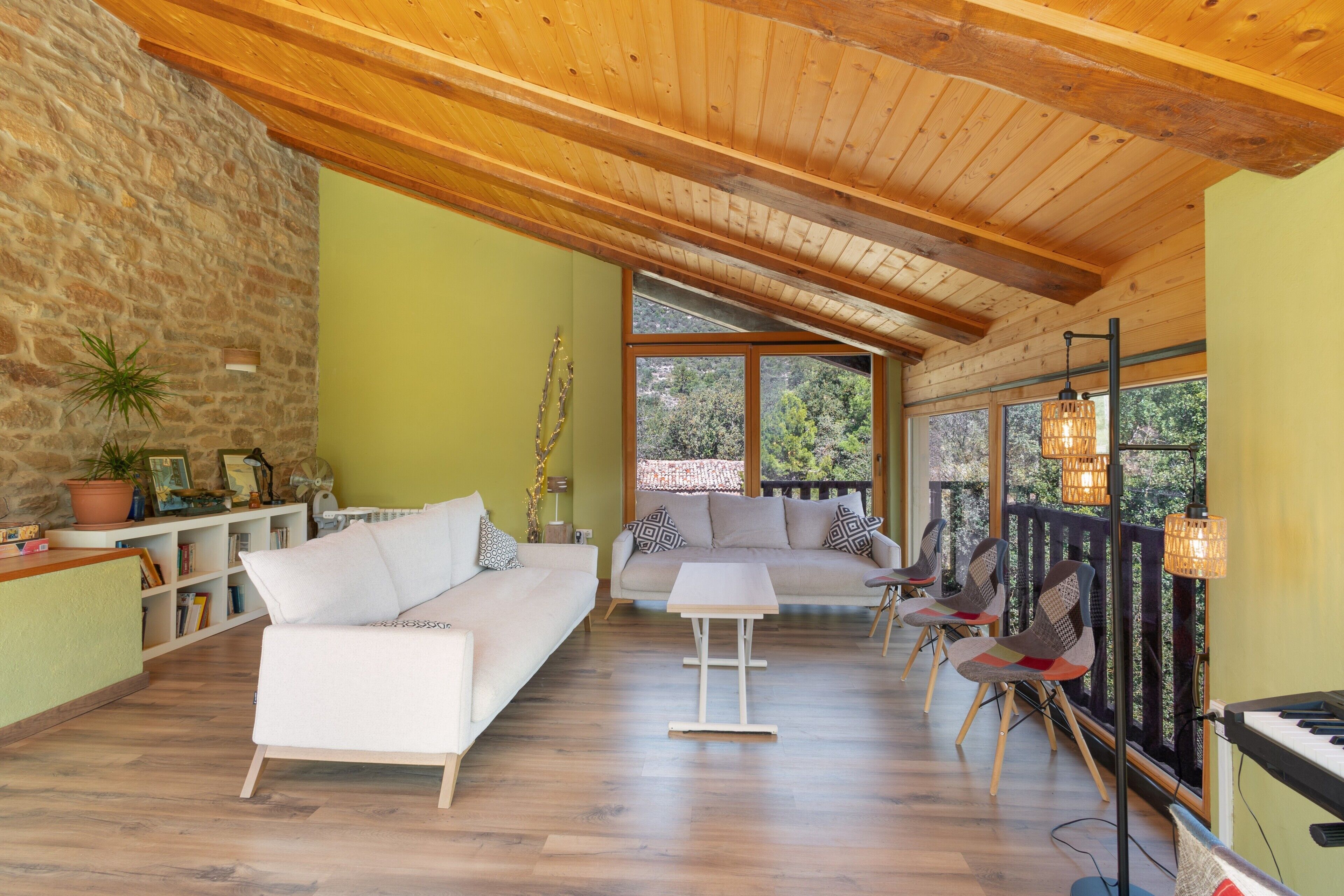 A spacious living area with a stone wall, wooden ceiling, and large windows offering a view of the outdoors.