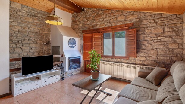 A living room with a stone wall, wooden ceiling, a fireplace, a television, and a sofa. - Chalet 'Masia La Clariana' with Mountain Views, Private Pool and Wi-Fi (Castelltallat)
