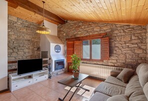 A living room with a stone wall, wooden ceiling, a fireplace, a television, and a sofa. - Chalet 'Masia La Clariana' with Mountain Views, Private Pool and Wi-Fi (Castelltallat)