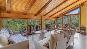 A spacious room with a high ceiling, large windows, and a view of a forest. There is a table with chairs and a keyboard. - Chalet 'Masia La Clariana' with Mountain Views, Private Pool and Wi-Fi (Castelltallat)
