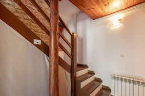A wooden staircase with a stone wall on one side and a white wall on the other, leading to a landing with a radiator. - Chalet 'Masia La Clariana' with Mountain Views, Private Pool and Wi-Fi (Castelltallat)