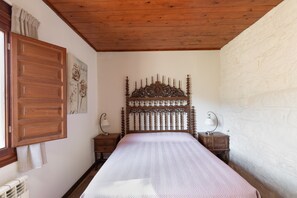 Ein Schlafzimmer mit einem hölzernen Kopfteil, einem Bett mit weißer Steppdecke, zwei Nachttischen mit Lampen, einem Heizkörper und einer Wand mit einem Blumenbild.