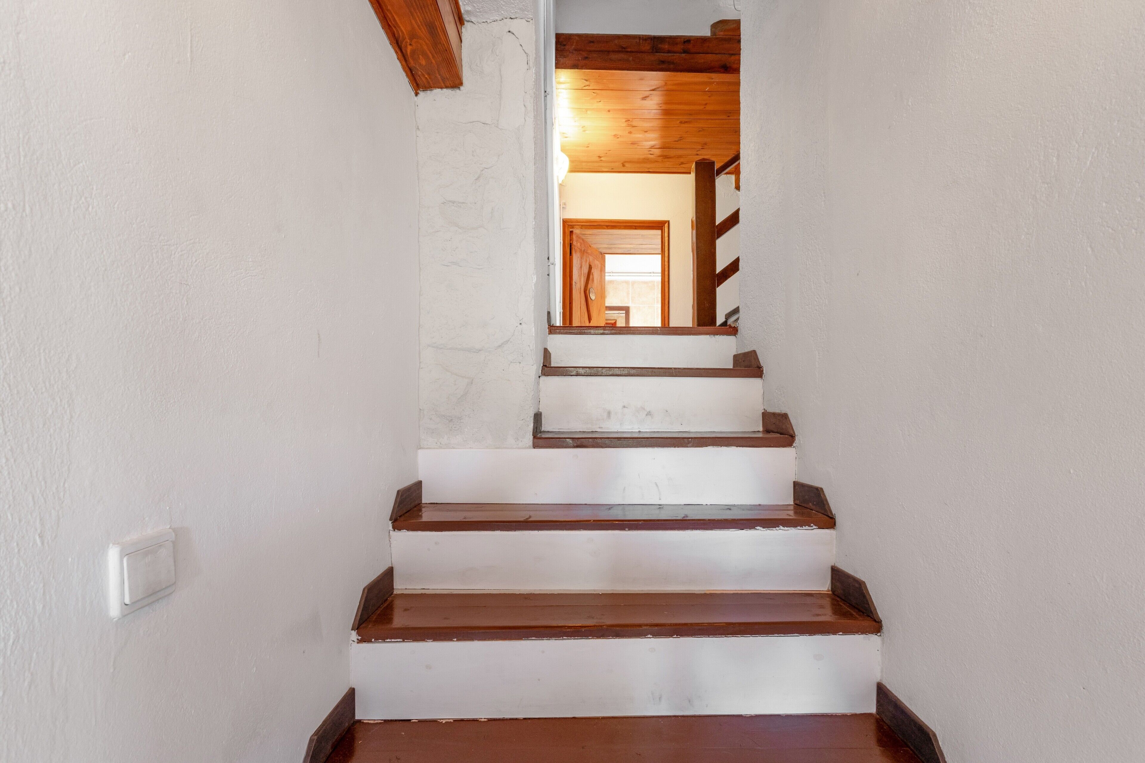 Una escalera de madera con paredes blancas que conduce a una puerta de madera.