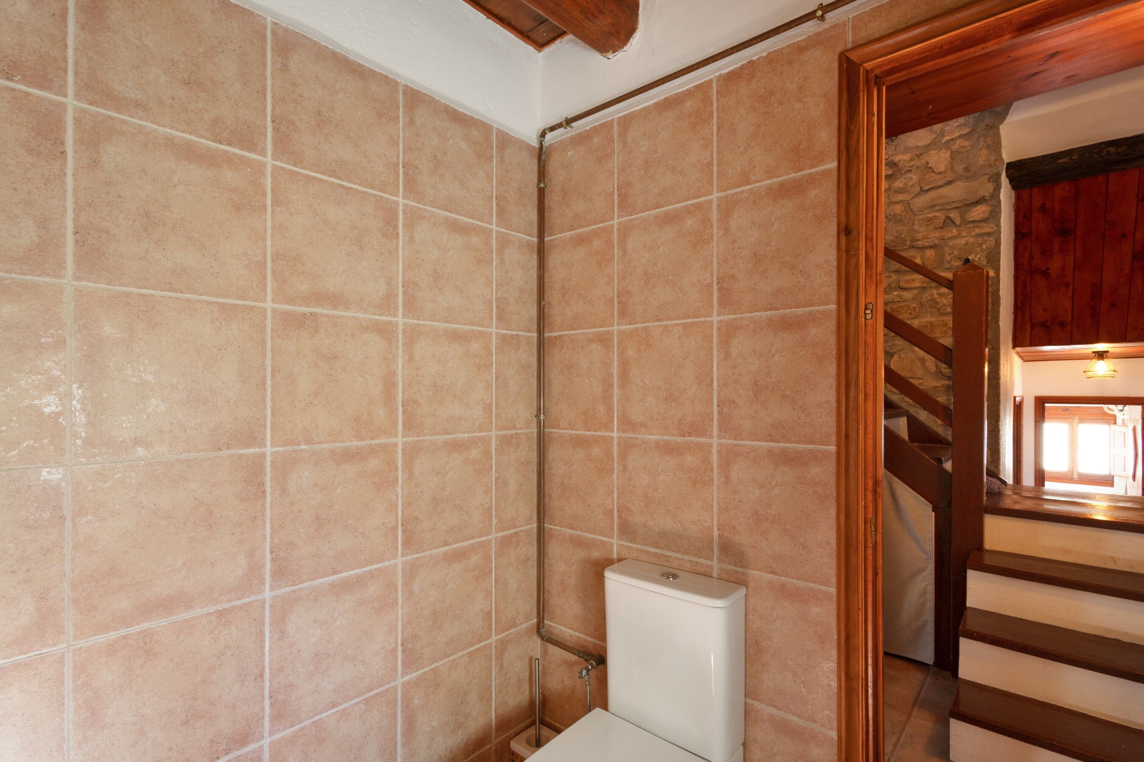 Ein Badezimmer mit beigen Fliesen, einer weißen Toilette und einer Holztreppe, die in einen anderen Raum führt.