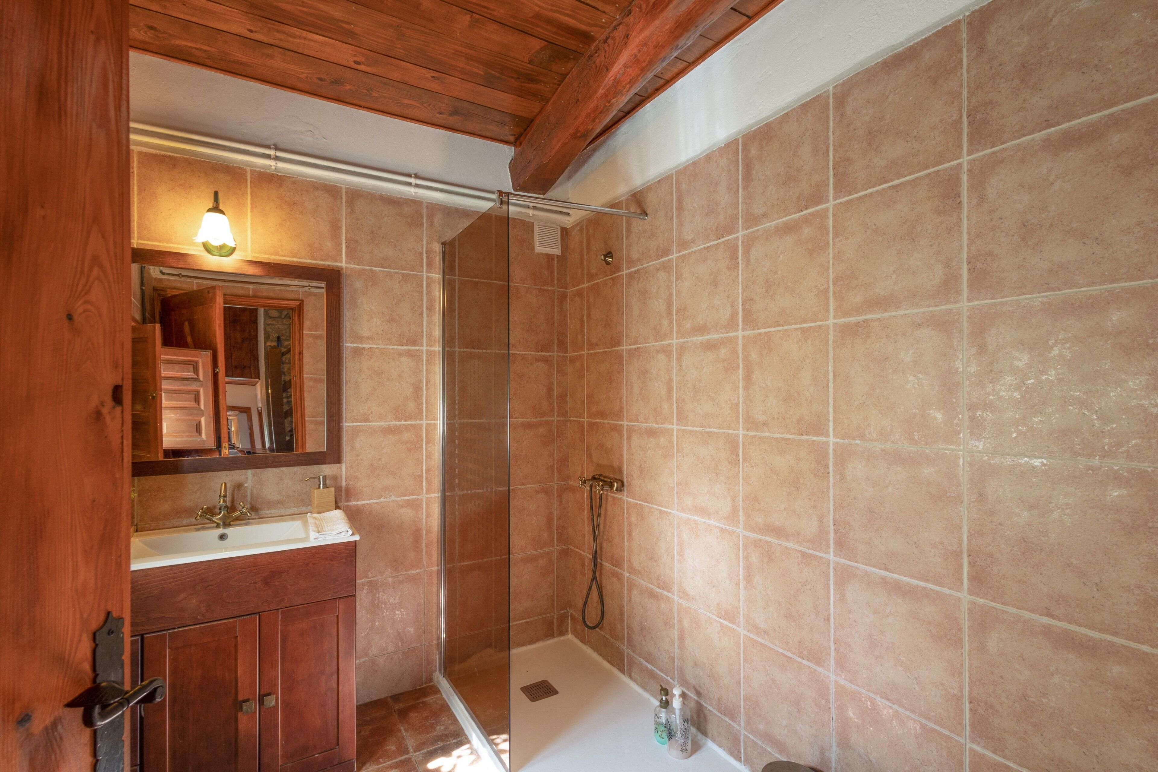 Un baño con tocador de madera, espejo, ducha y paredes con azulejos.