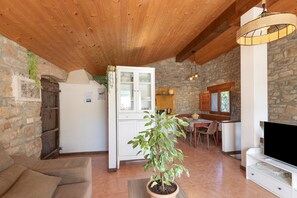 A cozy living area with a wooden ceiling, a stone wall, a dining table with chairs, a television, and a potted plant. - Chalet 'Masia La Clariana' with Mountain Views, Private Pool and Wi-Fi (Castelltallat)