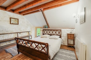 A bedroom with a wooden bed, stone walls, a sloped ceiling, and a small bedside table. - Holiday Home 'Maison Chapelle Du Verger' with Sea View, Shared Terrace and Private Garden (Cancale)