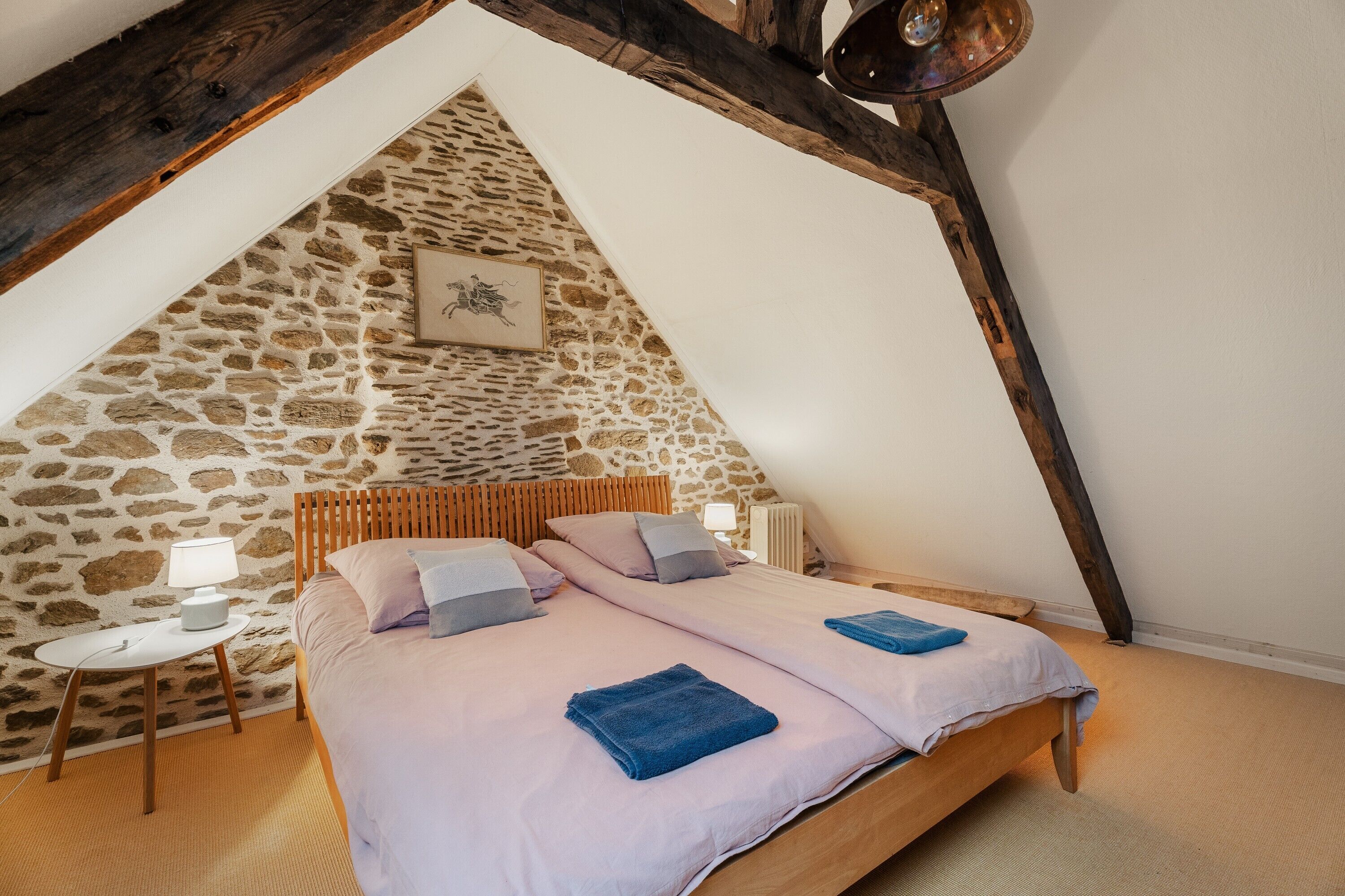 Een slaapkamer met een stenen muur, een houten bed, een klein nachtkastje en een foto aan de muur.