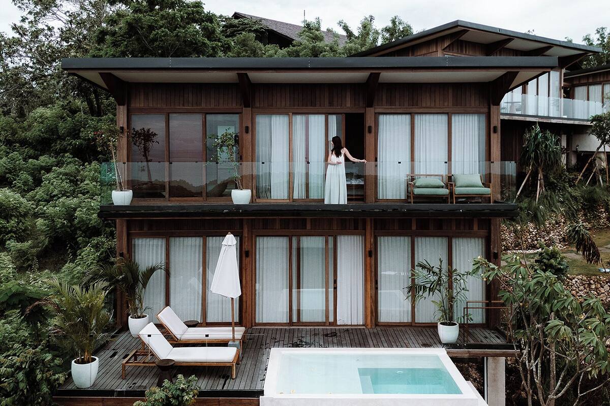 Ein modernes, zweistöckiges Haus mit Balkon, Pool und Liegestühlen.