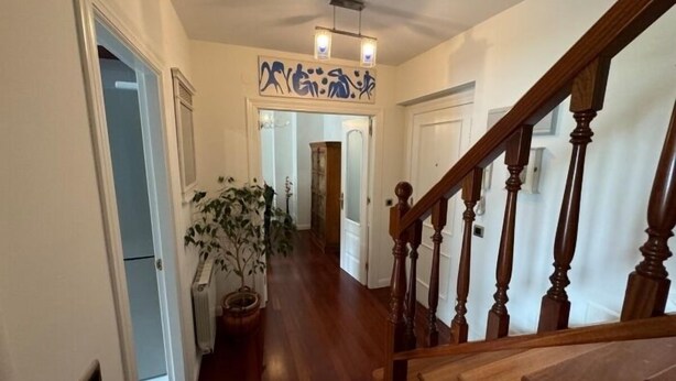 A wooden staircase with a handrail, leading to a landing with a potted plant and a wall-mounted light fixture. - Rental unit in Liencres · ★New · 3 bedrooms · 3 beds · 2 baths (Liencres)