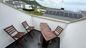A rooftop terrace with a wooden table and chairs, solar panels, and a view of surrounding buildings and hills. - Rental unit in Liencres · ★New · 3 bedrooms · 3 beds · 2 baths (Liencres)