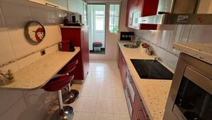 A kitchen with red cabinets, a white countertop, a stainless steel sink, and a built-in oven. - Rental unit in Liencres · ★New · 3 bedrooms · 3 beds · 2 baths (Liencres)