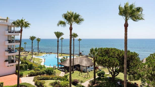 A resort with a swimming pool, palm trees, and a view of the ocean.