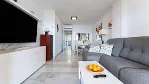 A modern living room with a flat-screen TV, a grey sofa, a coffee table with oranges, and a white cabinet.