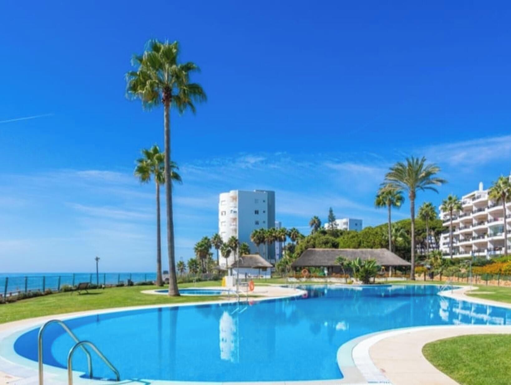 A resort with a large swimming pool, palm trees, and a view of the ocean.