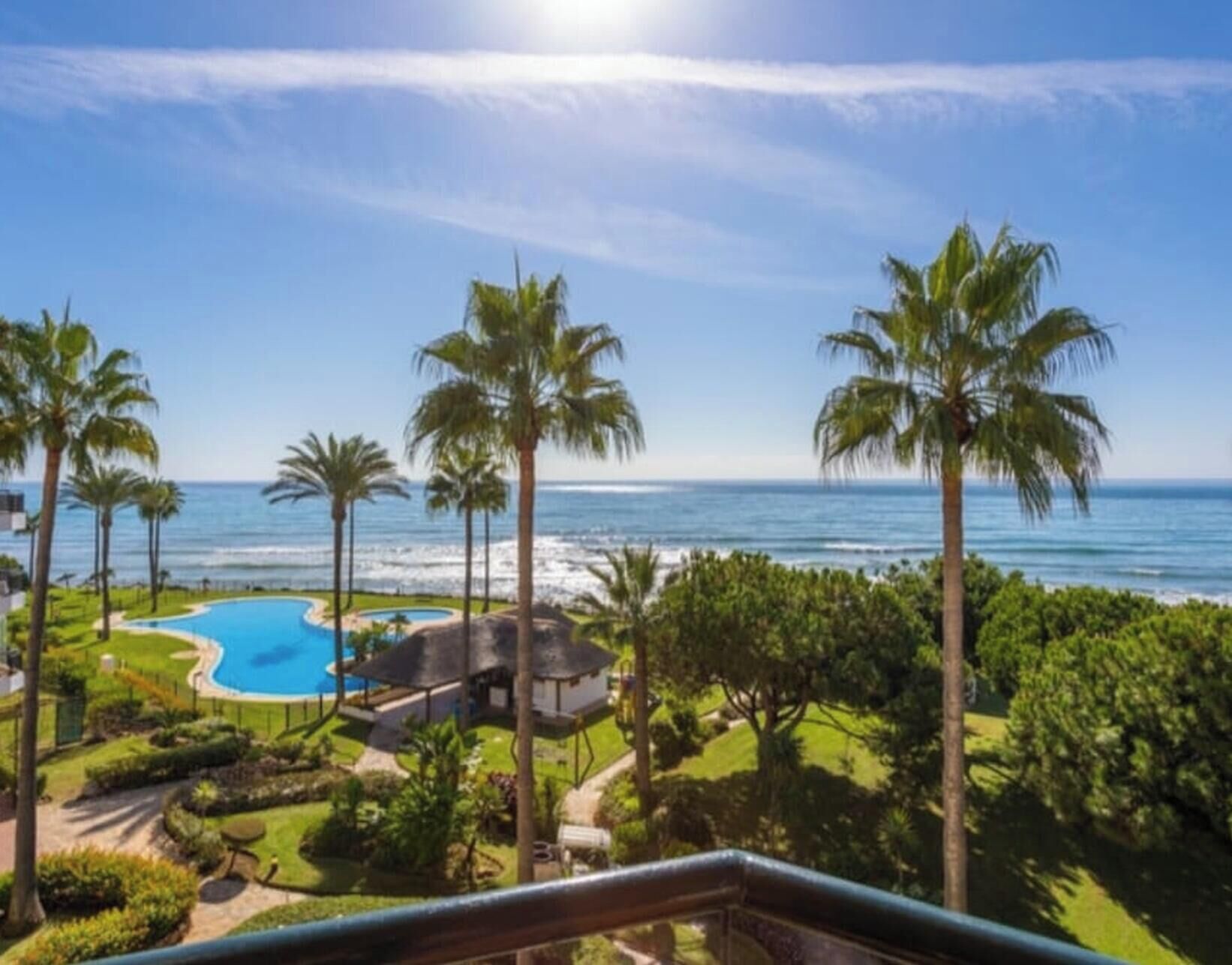 Ein Pool mit Blick auf den Ozean, Palmen und einen klaren Himmel.