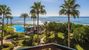 A pool with a view of the ocean, palm trees, and a clear sky.