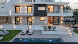 Une maison moderne à deux étages, dotée d’une piscine, d’un espace extérieur aménagé et d’un balcon bien éclairé.