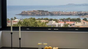 Une chambre avec vue sur une ville côtière, une table décorée de bougies et de citrons, et une fenêtre donnant sur la mer.