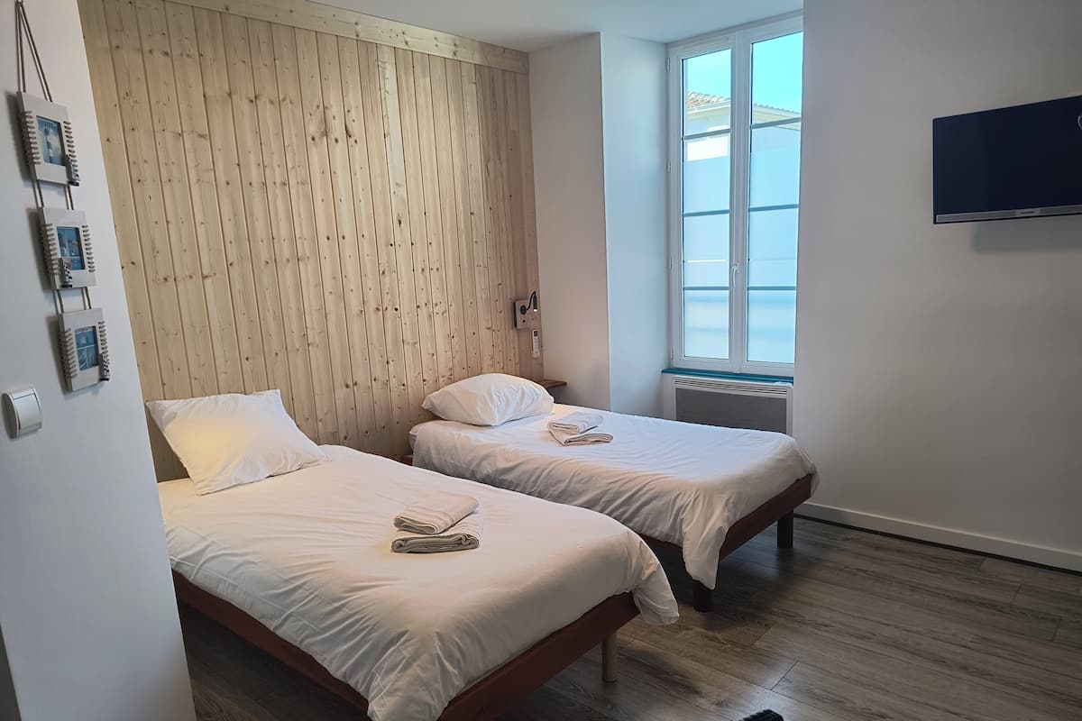A room with two beds, wooden paneling on the wall, a window, and a flat-screen TV.