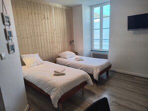 A room with two beds, wooden paneling on the wall, a window, and a flat-screen TV. - Hôtel Bar Restaurant La Marie Galante (Saint-Georges-d'Oleron)