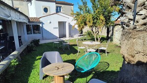 A courtyard with outdoor seating, a white building, and a tree with fruit. - Hôtel Bar Restaurant La Marie Galante (Saint-Georges-d'Oleron)