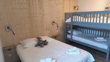 Un dormitorio con pared de madera, literas, una mesita de noche con lámpara, un osito de peluche y toallas dobladas con cuidado.
