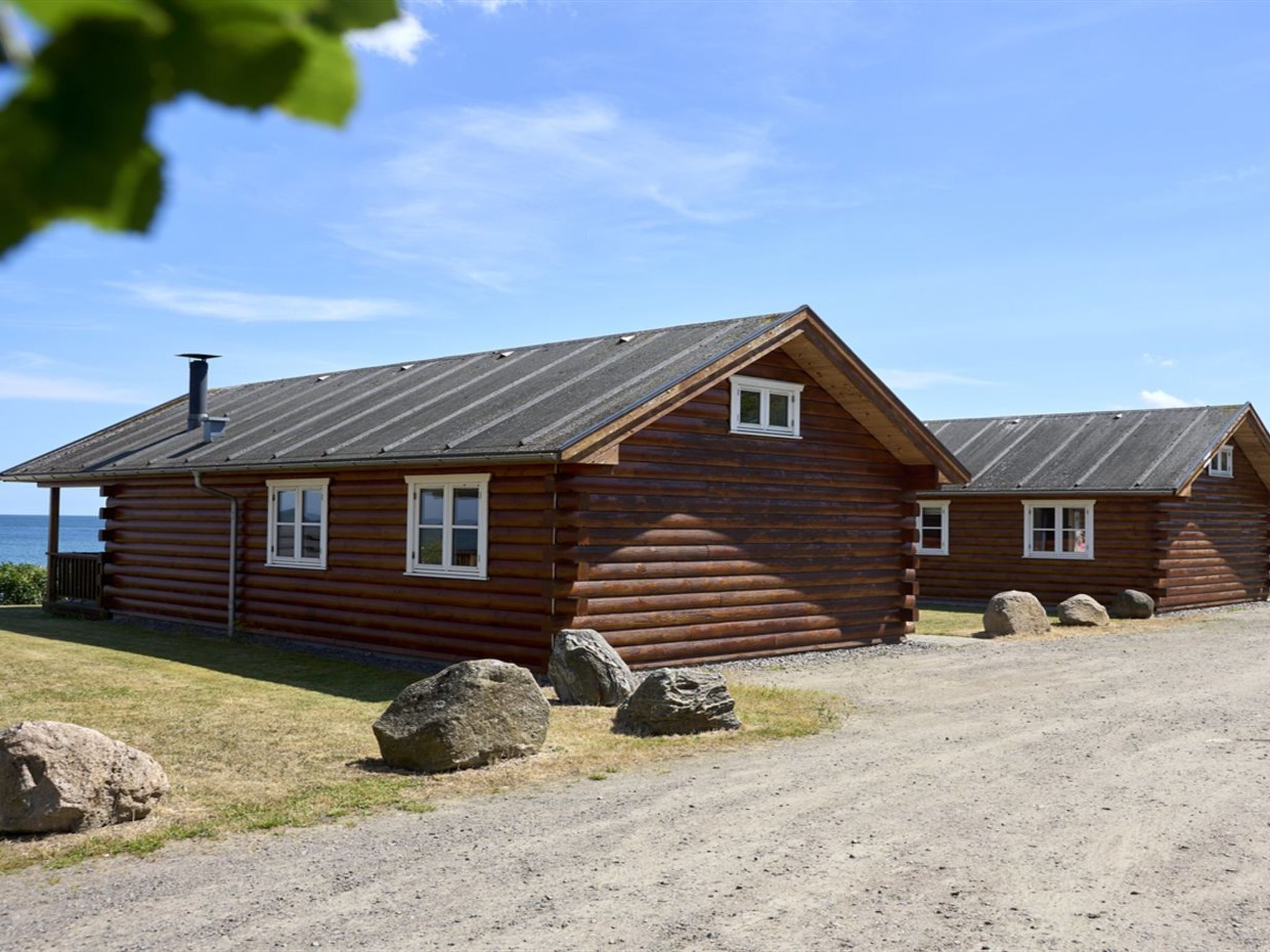 A log cabin with a metal roof, a chimney, and a small porch. There are large rocks in front of the cabin.