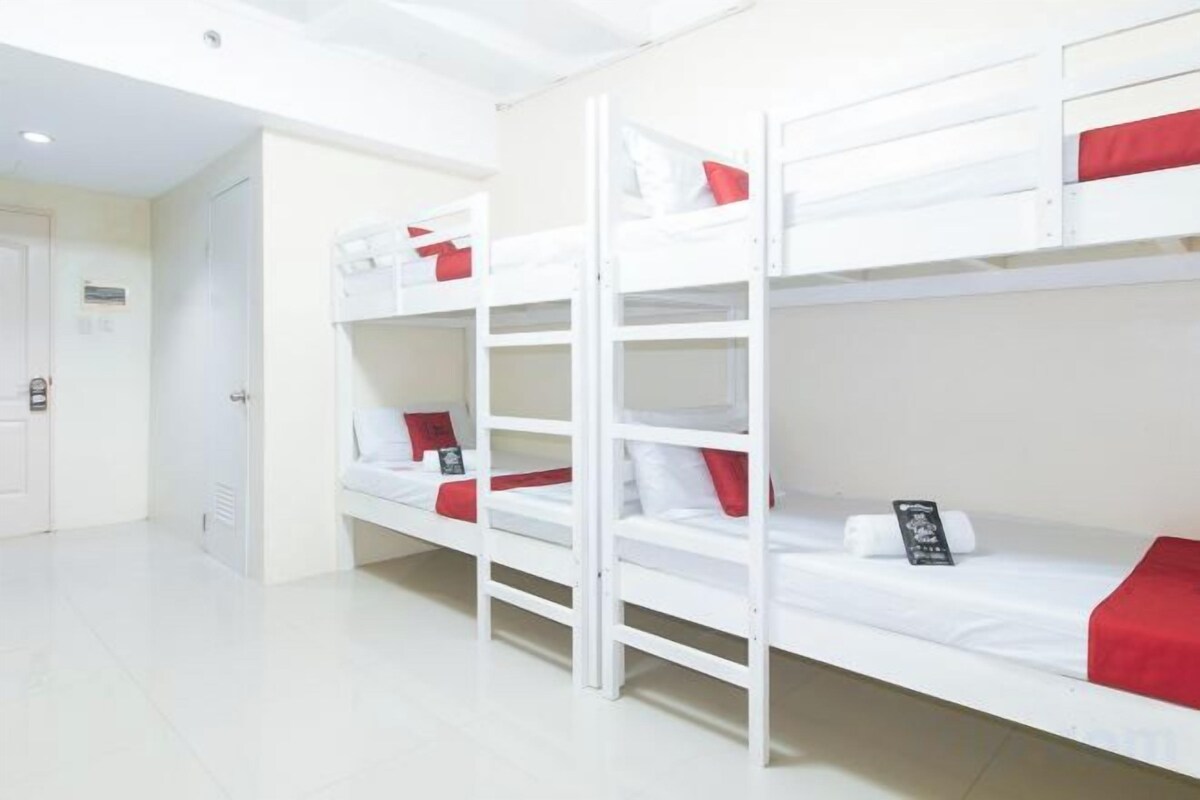 A bunk bed room with white bedding and red accents, a door, and a white floor.