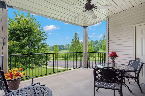 A covered balcony with a glass table and chairs, a potted plant, and a view of a green landscape. - 3 Bd 3ba Golf Condo in the Heart of Branson! Ticket Discounts (Branson)