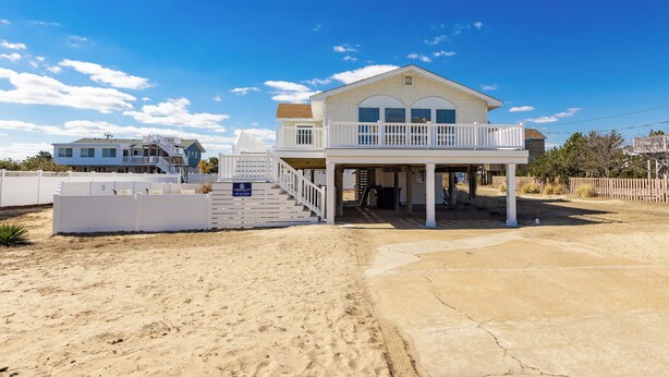 Ein zweistöckiges Strandhaus mit überdachter Veranda und einem eingezäunten Garten.