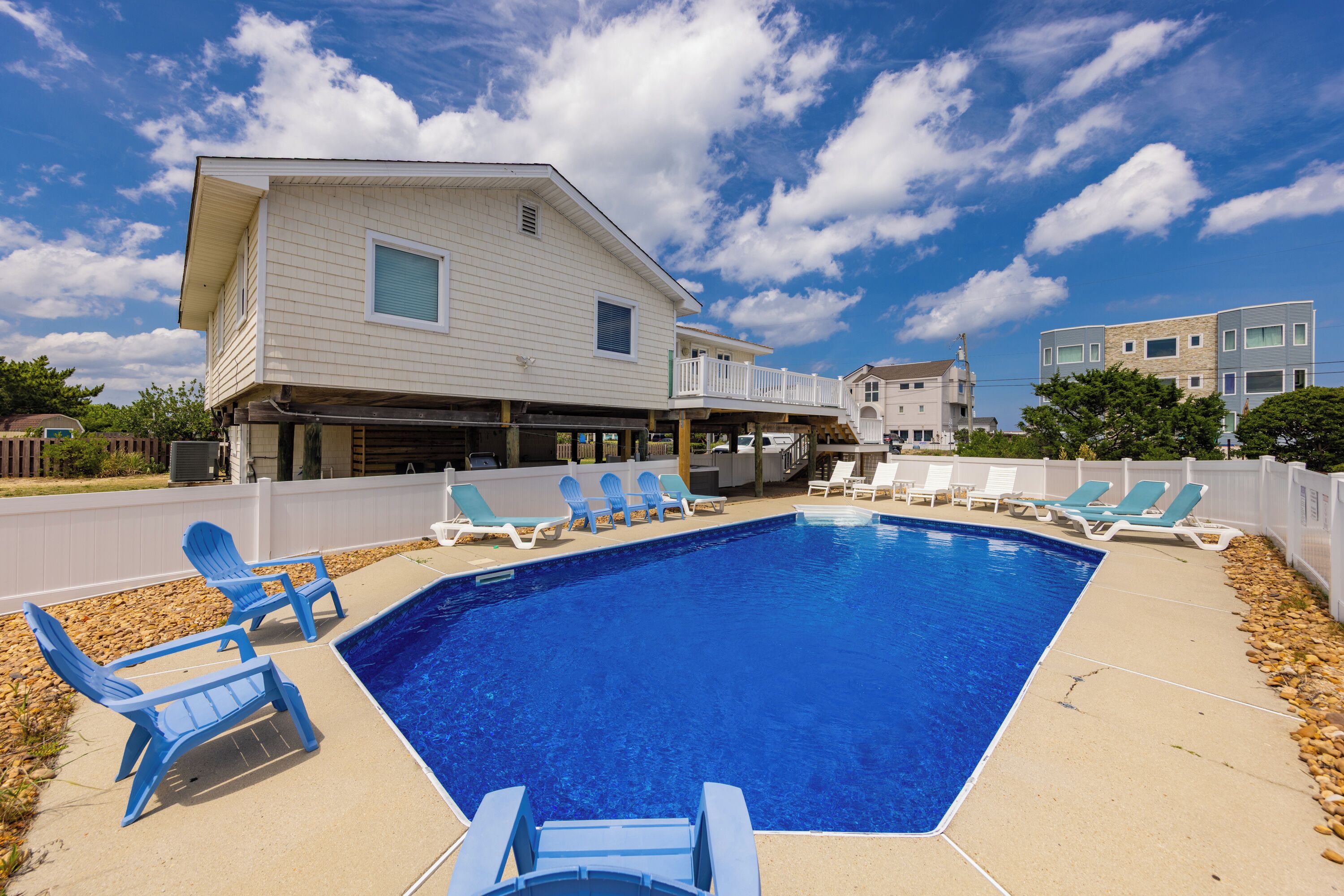Une piscine avec des chaises longues, une terrasse couverte et une maison à deux étages en arrière-plan.