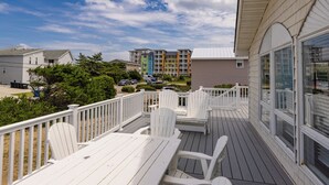 Eine Holzdielen-Terrasse mit weißen Stühlen und Tischen, mit Blick auf ein Wohngebiet mit bunten Mehrfamilienhäusern.