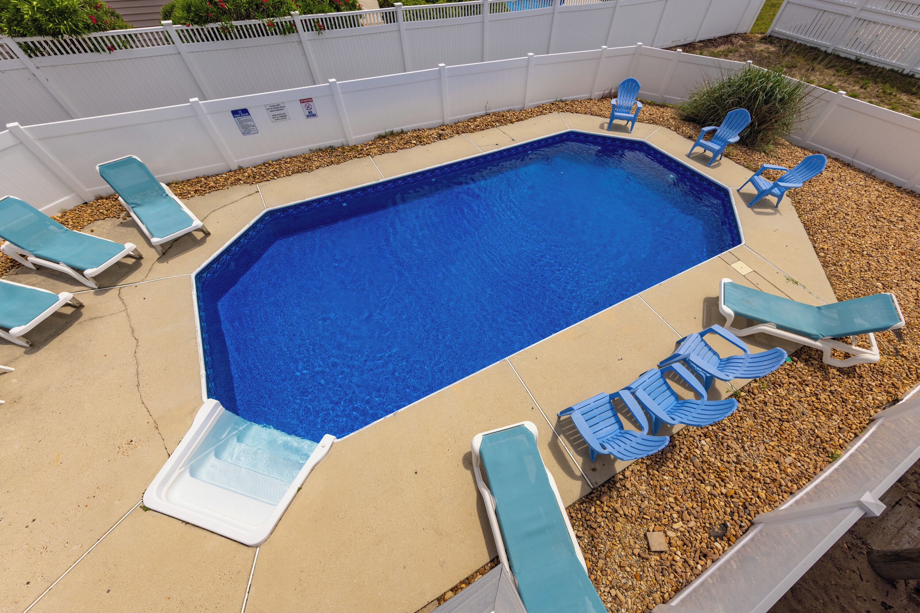 A rectangular swimming pool with a tiled deck, surrounded by a white fence.