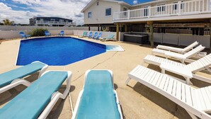 Ein Pool mit Liegestühlen, ein Grillplatz und ein zweistöckiges Haus im Hintergrund.