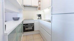 Cozinha compacta com armários brancos, forno embutido e cafeteira.