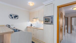 Cocina compacta equipada con microondas, estufa y lavabo. Pequeño comedor con mesa y sillas.